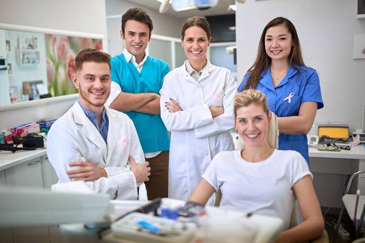 A group of dental hygiene students at Dental Hygienist School posing together in a clinical setting, showcasing teamwork and professional development.