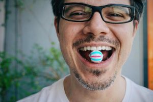 A man smiling with a colorful hard candy resting on his teeth, emphasizing that hard candies are the worst candy for your teeth due to their potential to cause dental damage.