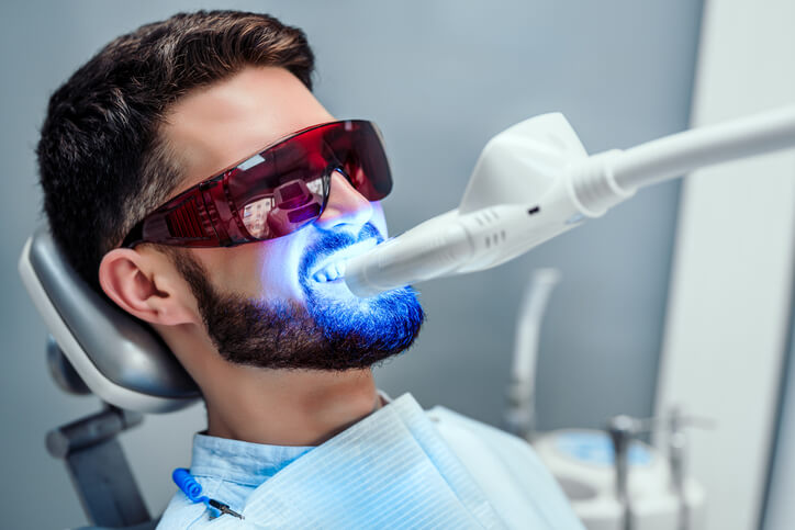 A dental hygienist training grad performing laser tooth whitening on a patient