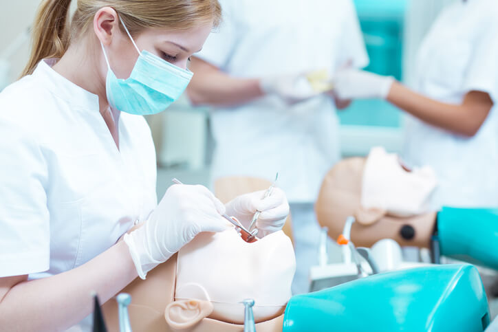 A dental assistant student practicing on a dental mannequin