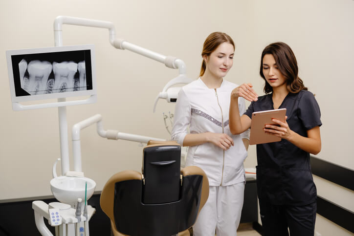 Two dental assistants review information on a tablet in a dental office, reflecting coordination and workflow support in dental assisting.