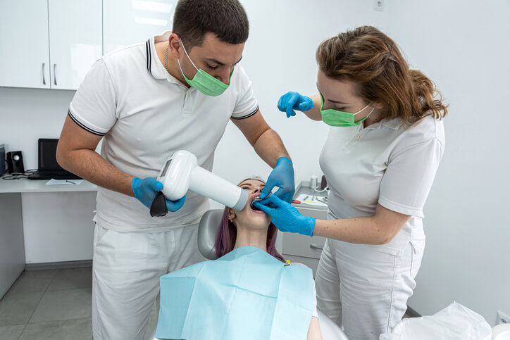 A clinical team works with a patient during a dental appointment, showing the chairside support typical of dental assisting.